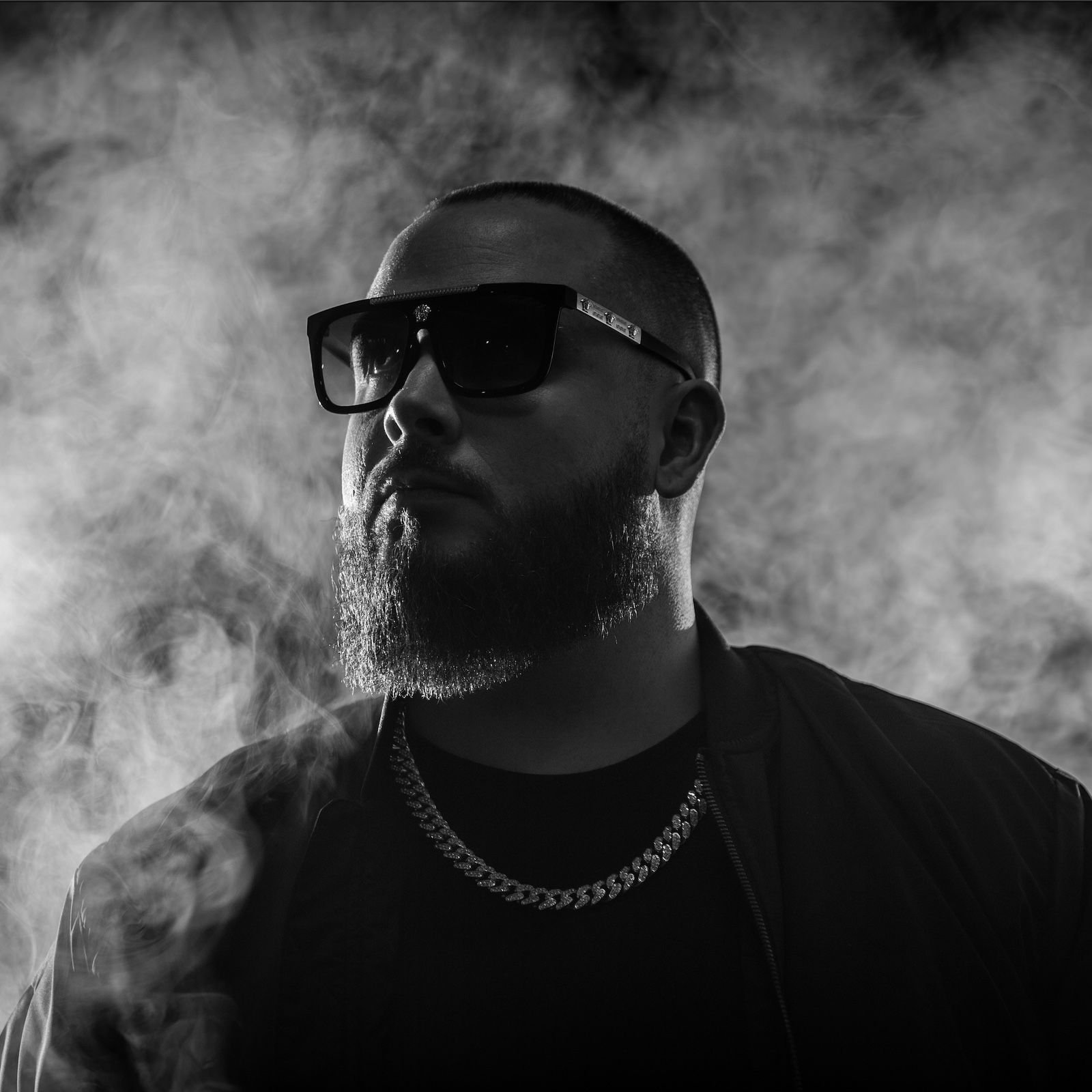 JSTN DMND in dark sunglasses and a chain, surrounded by smoke