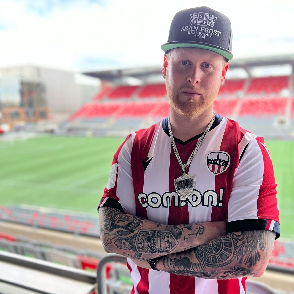 Sean Frost in an Atlético Ottawa jersey with arms crossed in the stands